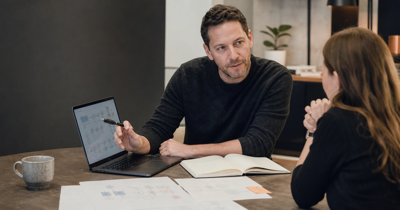 Editorial-style business decision scene showing a founder-operator reviewing workflow diagrams and software fit with an advisor.